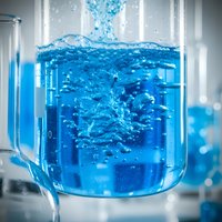 Blue liquid pouring into glass beaker with bubbles and splash in laboratory setting for scientific research and chemical experiments.