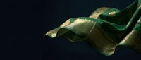Elegant flowing green silk fabric with golden highlights creating luxurious waves against dark background for premium textile and fashion design projects.