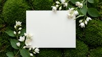 Blank white card surrounded by fresh green moss and delicate white flowers creating natural frame for wedding invitations or spring greeting cards.