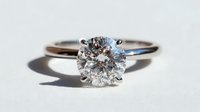 Elegant solitaire diamond engagement ring with round brilliant cut stone set in silver or white gold band on neutral background.