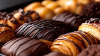 Assorted gourmet chocolate covered pastries and eclairs with dark and milk chocolate drizzle in close up view showing flaky layers and rich glazed details.