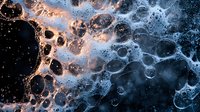 Mesmerizing macro photography of soap bubbles with dark blue and orange gradient background creates abstract cosmic pattern with light reflections and bokeh effect.