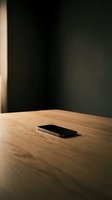Smartphone lying on wooden table with dark wall background, minimalist composition with warm lighting for technology and business concepts.