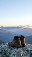 Worn hiking boots on rocky summit overlooking misty mountain ranges at dawn with soft pastel sky and layered peaks in distance for outdoor adventure concepts.