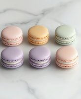 Colorful French macarons in pastel pink, peach, mint green and lavender arranged on white marble background. Sweet meringue cookies with cream filling.