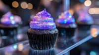 Chocolate cupcake with vibrant purple and blue sparkly frosting on dark background with bokeh lights creates magical dessert atmosphere for party celebration.