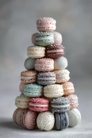 Colorful macarons stacked in pyramid shape with pastel pink, mint, cream, and lavender colors, decorated with silver sprinkles on gray background.