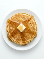 Stack of golden-brown pancakes topped with melting butter on white plate, ready for breakfast or brunch dining.