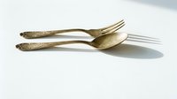 Elegant vintage brass fork and spoon set with ornate decorative handles on clean white background, isolated cutlery for kitchen and dining design projects.