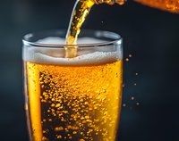 Pouring golden beer into glass with bubbles and foam on dark background, close up macro shot capturing carbonation and refreshing beverage movement.