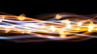 Glowing light trails with orange and white streaks flowing in dynamic waves against black background create abstract luminous effect for technology designs.