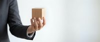 Businessman in dark suit holding small cardboard box, isolated on white background for delivery, shipping, logistics, and business concepts.