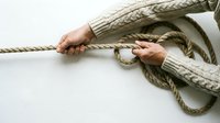 Hands in beige knit sweater tying natural jute rope into knot on white background. Crafting, sailing, climbing, teamwork and problem-solving concept.