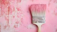 Wide paintbrush with white bristles and metal ferrule on textured pink concrete wall background, minimalist composition for renovation and decoration concepts.
