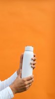 Hand holding white cosmetic bottle against vibrant orange background for product mockup, advertising, skincare, beauty, wellness, and promotional campaigns.