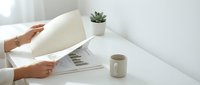 Unrecognizable woman arranging papers on white desk with succulent plant and coffee mug in bright workspace.