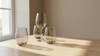 Elegant wine glasses on wooden table with natural sunlight streaming through window creating warm shadows in minimalist interior setting.