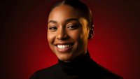 Young African American woman smiling confidently in black turtleneck against warm red background for business and lifestyle content.
