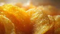 Extreme close up macro shot of crispy golden potato chips with visible salt crystals and textured surface in warm lighting, creating appetizing food background.