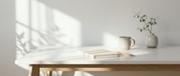 Wooden desk with open book, ceramic pitcher, dried flowers in vase, and window light casting shadows on white wall. Minimalist workspace for creative projects and design layouts.
