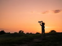Father lifting young child on shoulders at sunset in rural field, golden hour family bonding moment outdoors.
