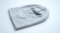 Gray knit beanie hat lying flat on white background, soft fabric winter accessory, casual cold weather headwear for fashion and retail use.