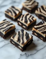 Chocolate brownies with cream cheese swirl in zebra pattern on marble surface. Close up view of homemade dessert squares shows rich texture and artistic decoration.