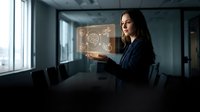 Woman in business attire holding glowing digital interface with gear icons, representing technology, innovation, and corporate solutions in modern office setting.