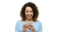 Young woman with curly brown hair and medium complexion, wearing light blue casual shirt, smiling while holding smartphone. Isolated on white background for app, technology, communication design use.