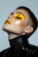 Young woman with striking golden yellow makeup and glossy lips in profile pose wearing black leather jacket for fashion and beauty concepts.