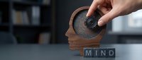 Man's hand rotating wooden gear inside human head silhouette with mind text blocks, representing mental process, creativity, and cognitive development for business and psychology concepts.