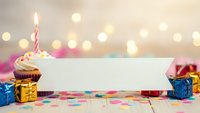 Birthday celebration scene with cupcake, candle, blank banner and colorful gift boxes on confetti background with bokeh lights for party invitations.
