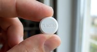 Hand holding white round placebo pill tablet between fingers against blurred medical background for pharmaceutical research and clinical trials.