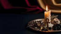 Burning candle on ornate metal tray with melted wax drips creates atmospheric mood lighting for relaxation and meditation in dark cozy interior setting.