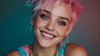 Young woman with pink pixie haircut and bright blue eyes smiling against teal background, showcasing colorful style and dangling earrings.
