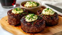 Grilled beef tenderloin steaks topped with herb compound butter and fresh chives on wooden cutting board. Juicy meat with caramelized crust and melting butter.