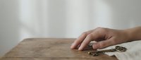 Hand reaching for house keys on wooden table surface with soft natural lighting and neutral background for real estate concepts.