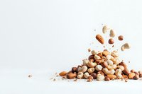 Mixed nuts falling and creating pile on white background, including cashews, almonds, hazelnuts and macadamia. Isolated composition with copy space.