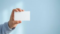 Hand holding blank white business card against light blue background, ideal for corporate branding and marketing mockups.