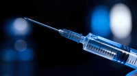 Medical syringe with needle on dark blue background with bokeh lights for healthcare and vaccination concepts in clinical settings.
