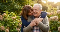 Happy senior Caucasian couple embracing in blooming garden during golden hour sunset, showing love and affection in their retirement years together.