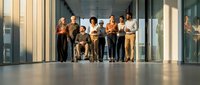Diverse business team standing together in modern office corridor with natural lighting and glass walls for corporate teamwork concepts.