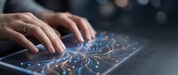 Close-up of hands typing on illuminated futuristic keyboard with glowing blue circuit patterns and light effects, representing technology, digital communication, and modern computing.