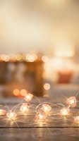 Warm golden string lights with decorative metal orbs glowing on rustic wooden surface creating cozy atmospheric bokeh background for holiday celebrations.