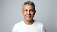 Smiling middle-aged Hispanic man with gray hair wearing white t-shirt on neutral background for business and lifestyle concepts.