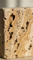 Weathered travertine stone block with natural holes and porous texture showing geological formation and erosion patterns in warm beige tones.
