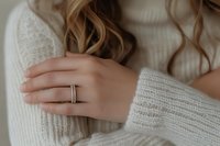 Close up of feminine hands with elegant engagement ring wearing cozy white knitted sweater, soft natural lighting creates romantic atmosphere.