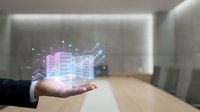 Businessman holding holographic financial charts and data analytics above palm in modern conference room.