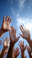 Multiple hands raised up reaching toward bright blue sky with white clouds expressing unity hope and community spirit in outdoor setting.