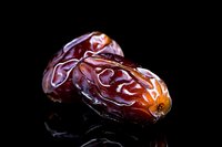 Fresh ripe dates with glossy skin on black reflective surface, dramatic lighting highlights natural texture and deep brown color. Macro food photography.